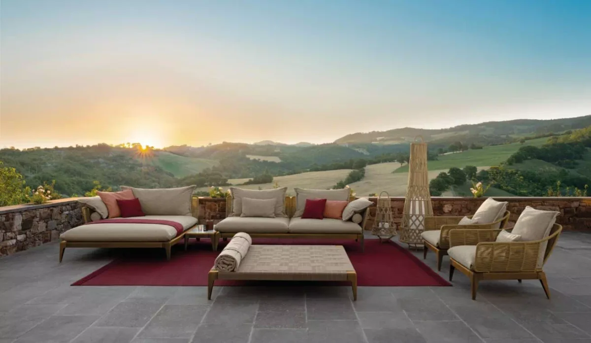 Divano modulare in teak e corda con cuscini ecrù ambientato su una terrazza aperta tra le colline al tramonto